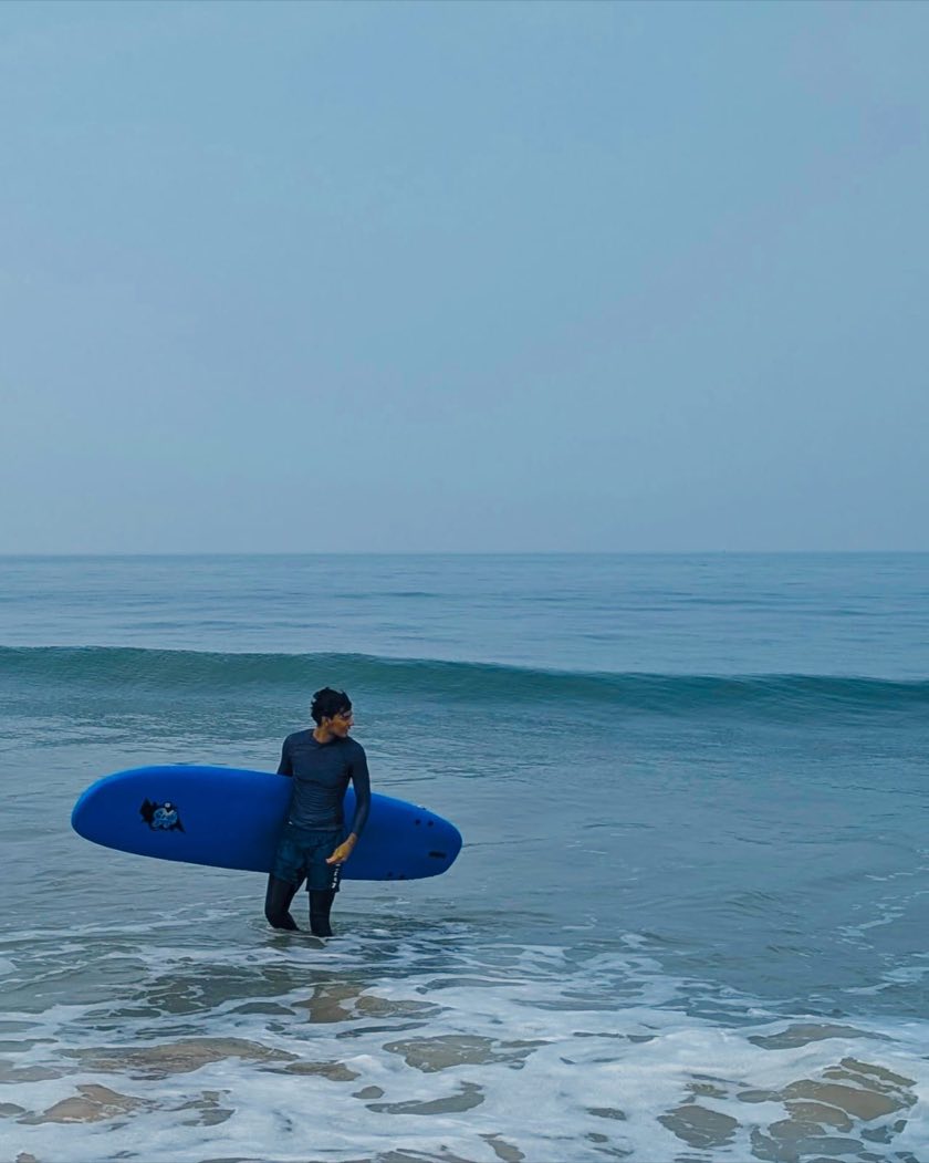 Nimitt walking out of the sea carrying a surfboard in Mulki, Karnataka