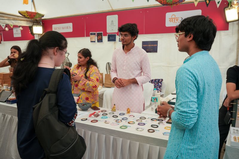 Nimitt in a pink kurta behind the Neer Ratna stall at a flea market, bracelets laid out on the table